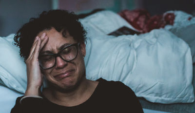 Woman sitting on the floor by her bed crying and wishing she would stop hurting.