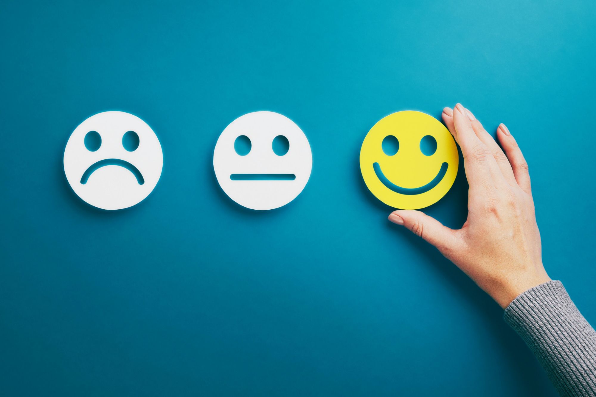 Depicting Finding Hope Is The Key To Moving On After Divorce with a sad face icon, a neutral face icon and a yellow happy face icon in a row on a blue background. A hand is adjusting the happy face to signify hope.