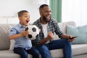Parenting advice for co-parenting after a divorce with father and young son excitedly watching a soccer game while at home one the couch.