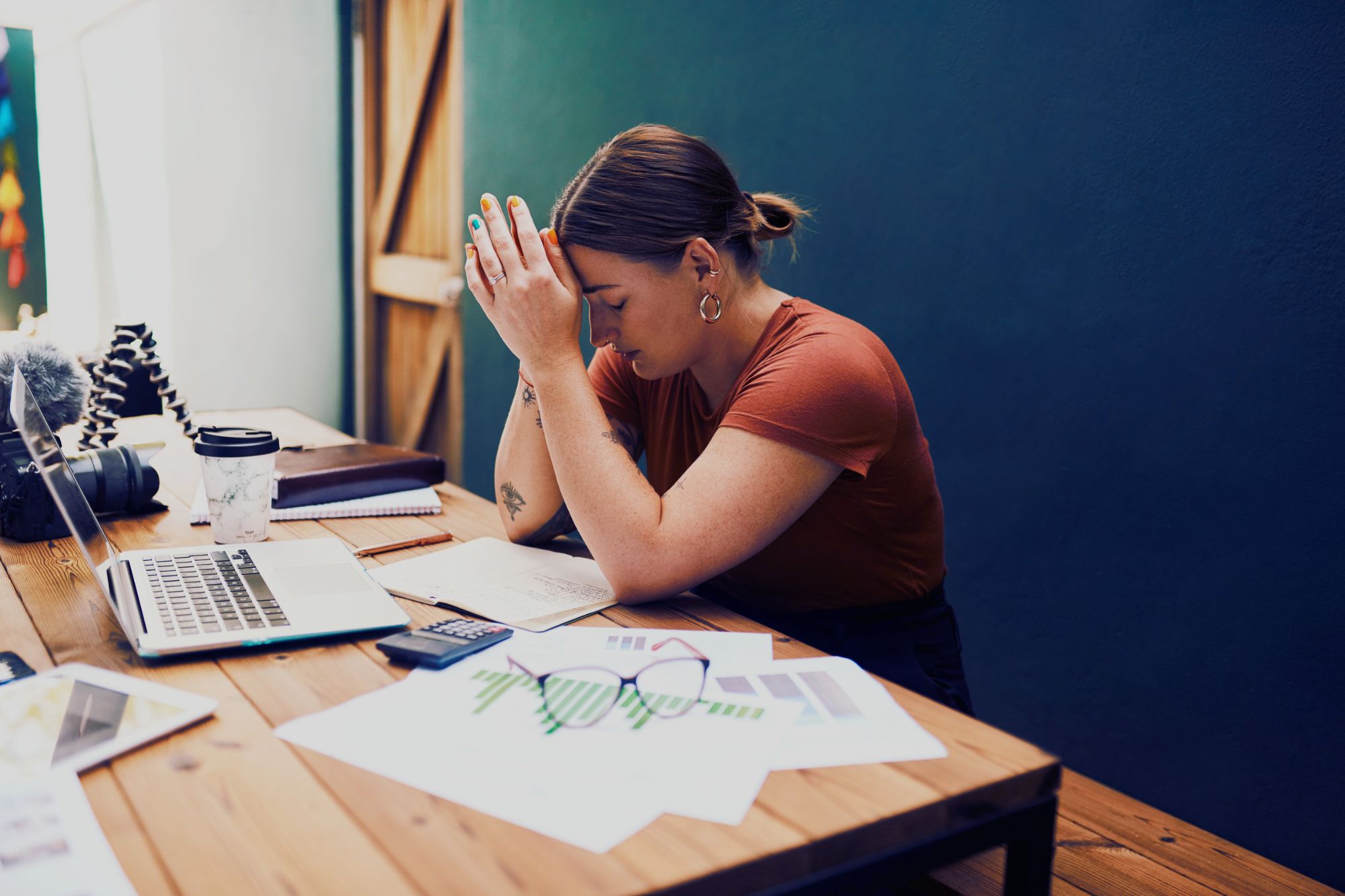 A sad woman sits at a desk with her head in her hands as she contemplates 4 Tips For Decreasing The Cost Of Divorce