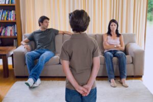 Father and mother sit on opposite sides of the couch as son stands watching them figure out How To Effectively Co-Parent With A Bully During Divorce