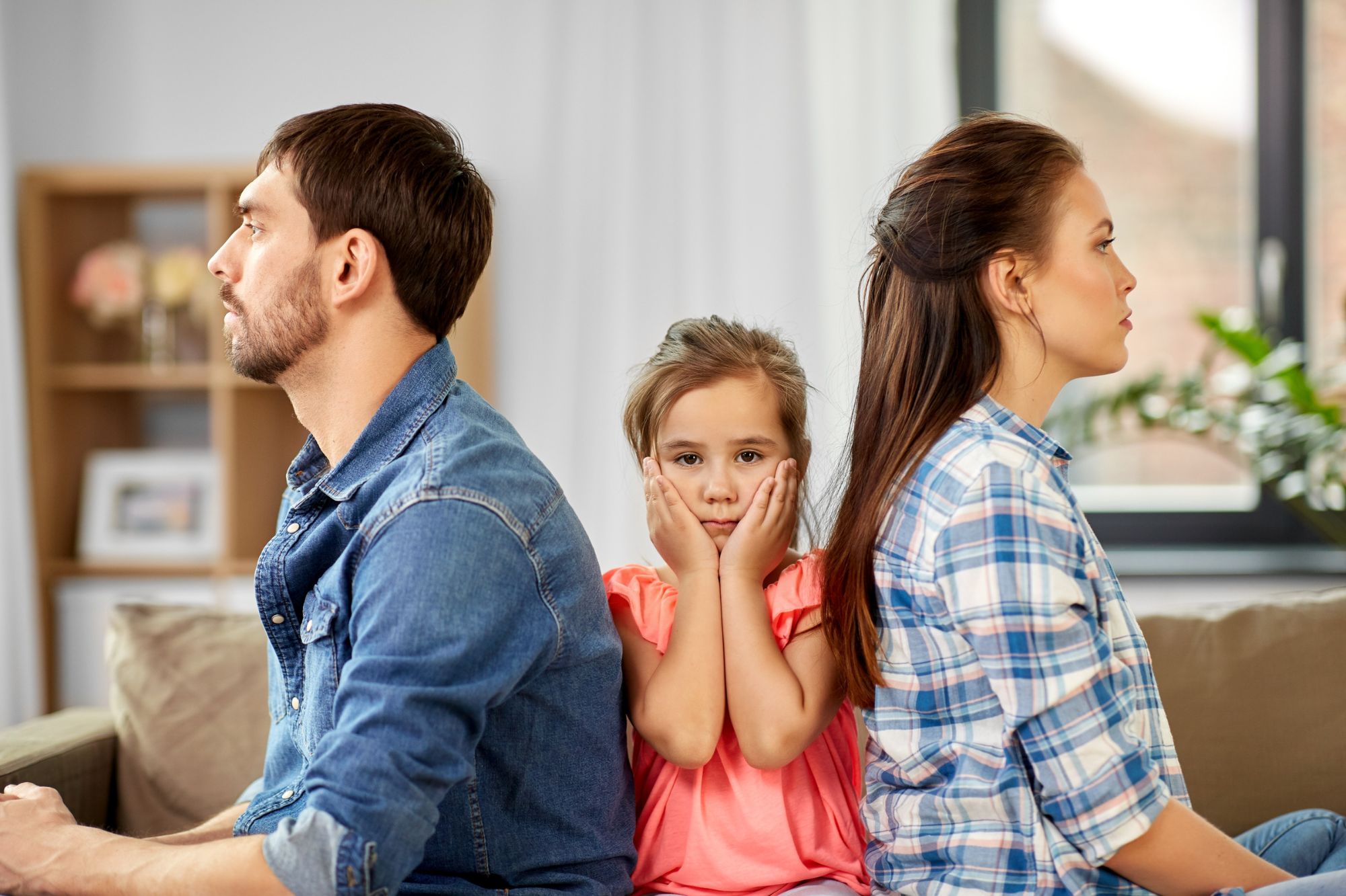 Child stuck in the middle as mom and dad sit back to back showing brutal signs that they hate each other more than they love their kids