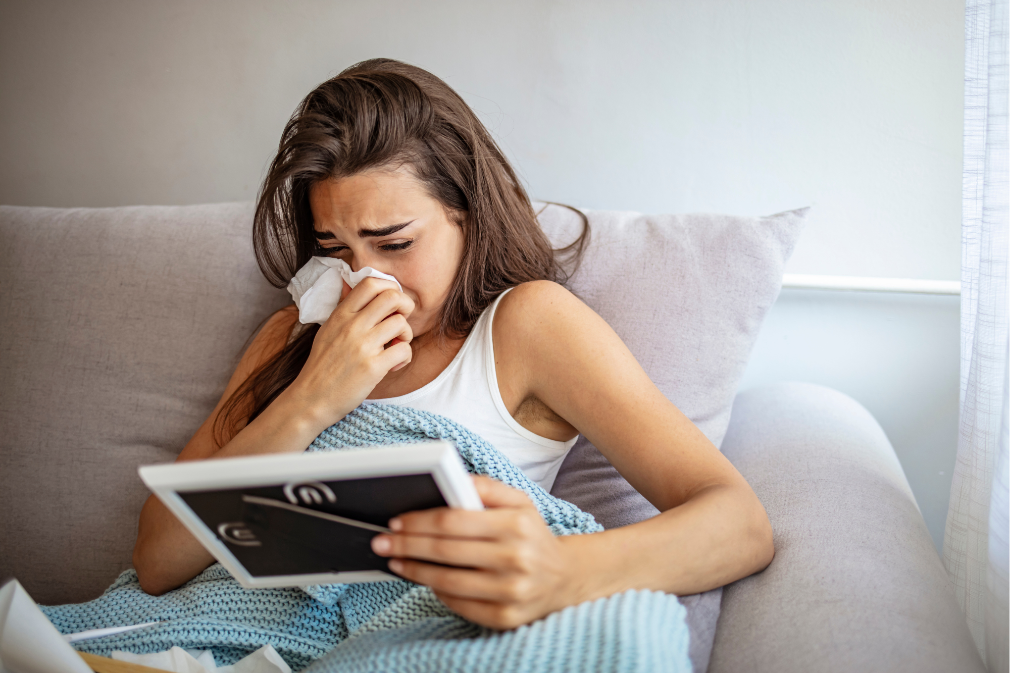 Woman on couch in blue blanket crying while looking at photograph