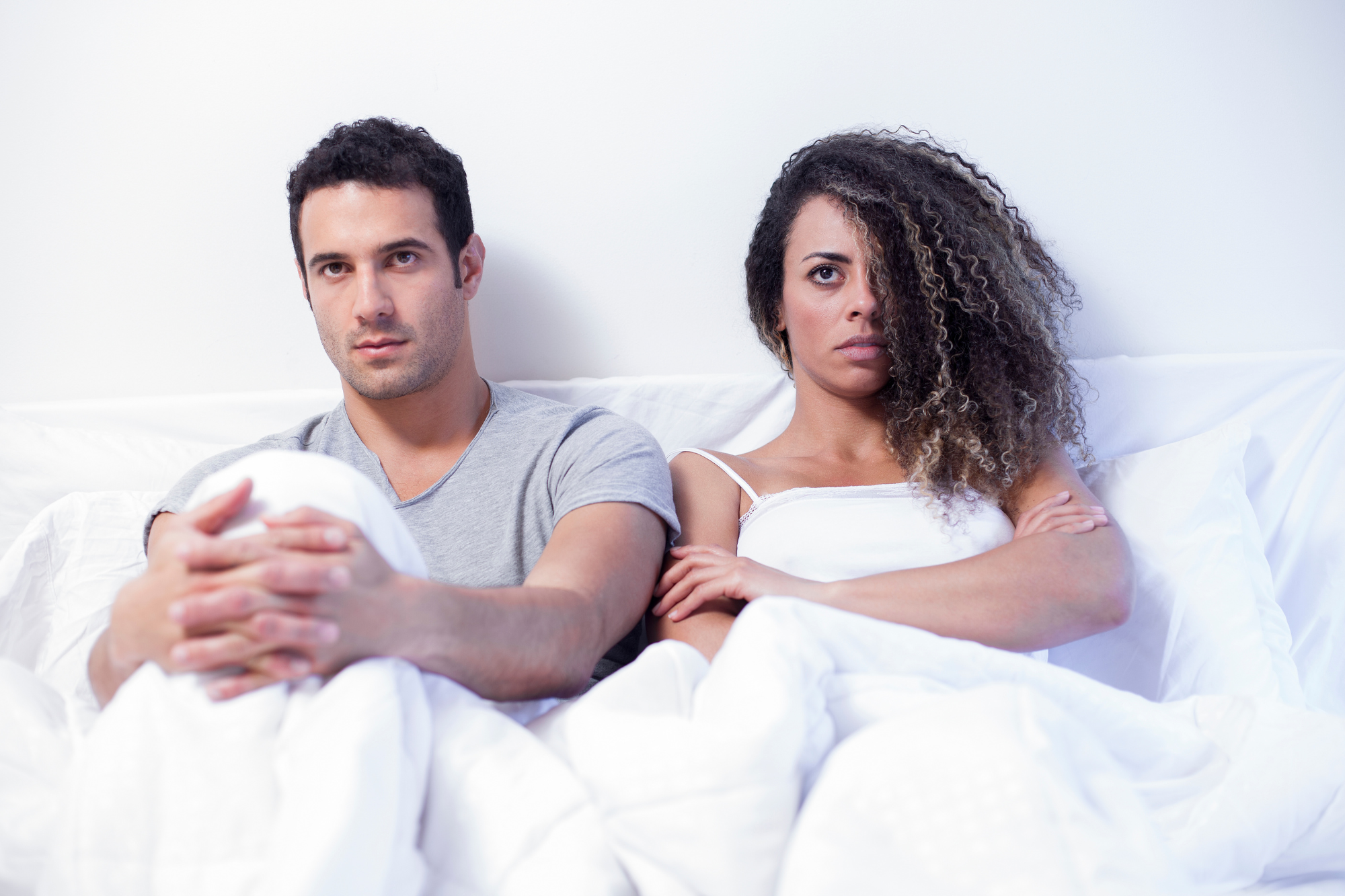 Angry couple in white bed not looking at each other. Six reasons couples do go to bed angry, on purpose.