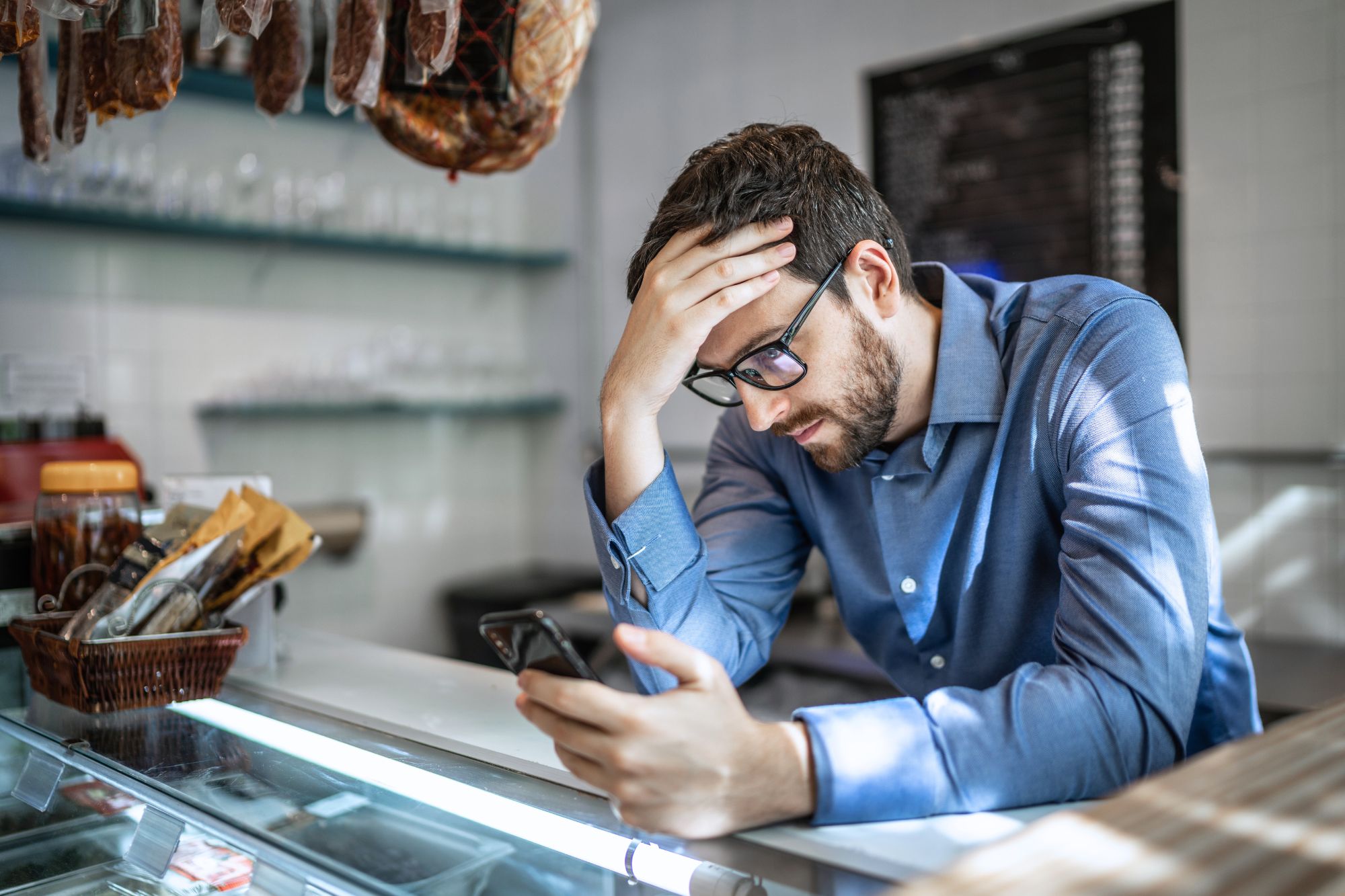 Man in blue shirt sits at a counter with head in his hand as he contemplates the tough questions you must ask yourself before leaving your marriage.