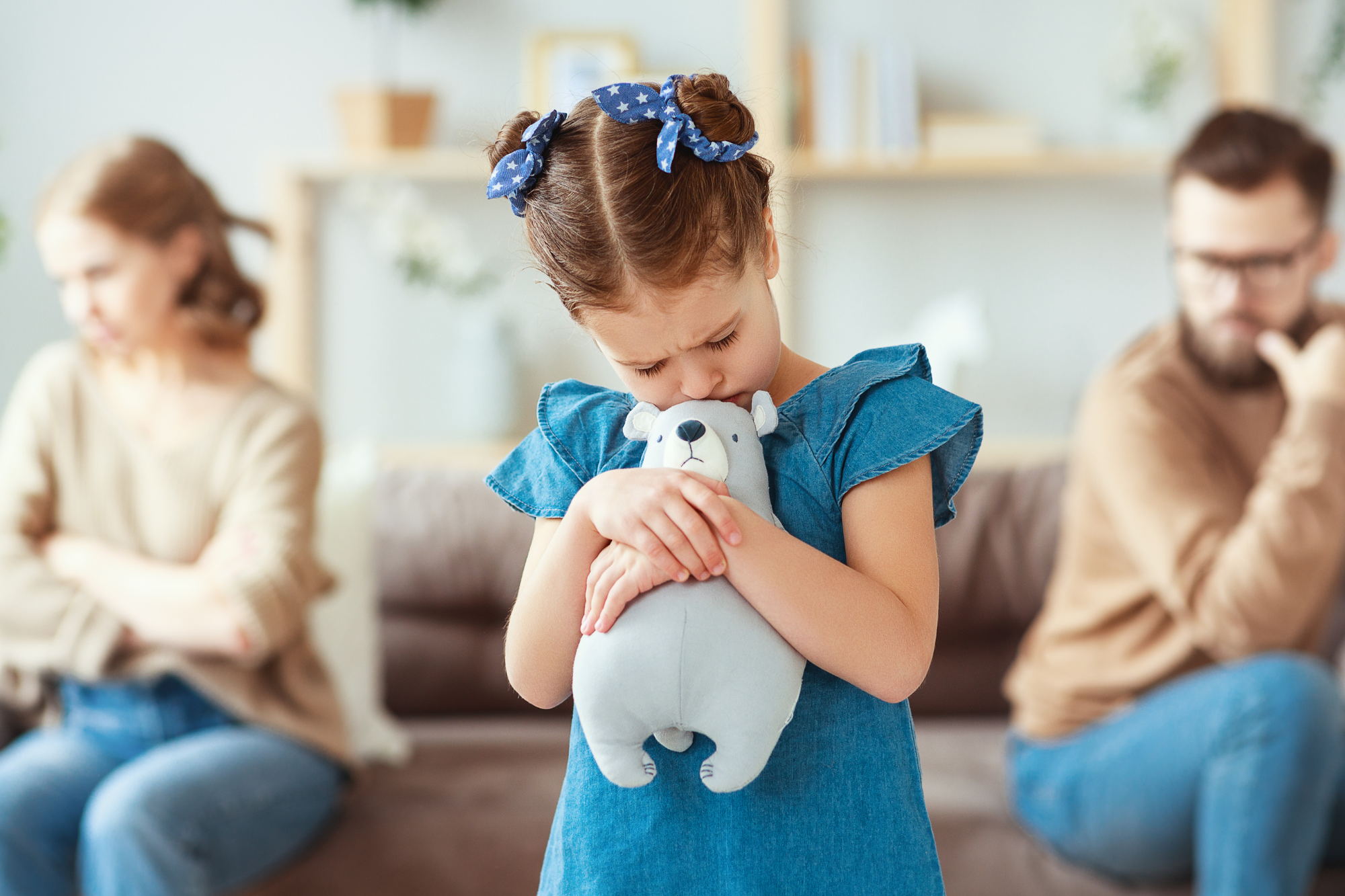 Sad little girl in blue holding stuffed animal while parents in background look away from each other. Nine ways a Man Can make a Decision to Divorce the Mother of his Children