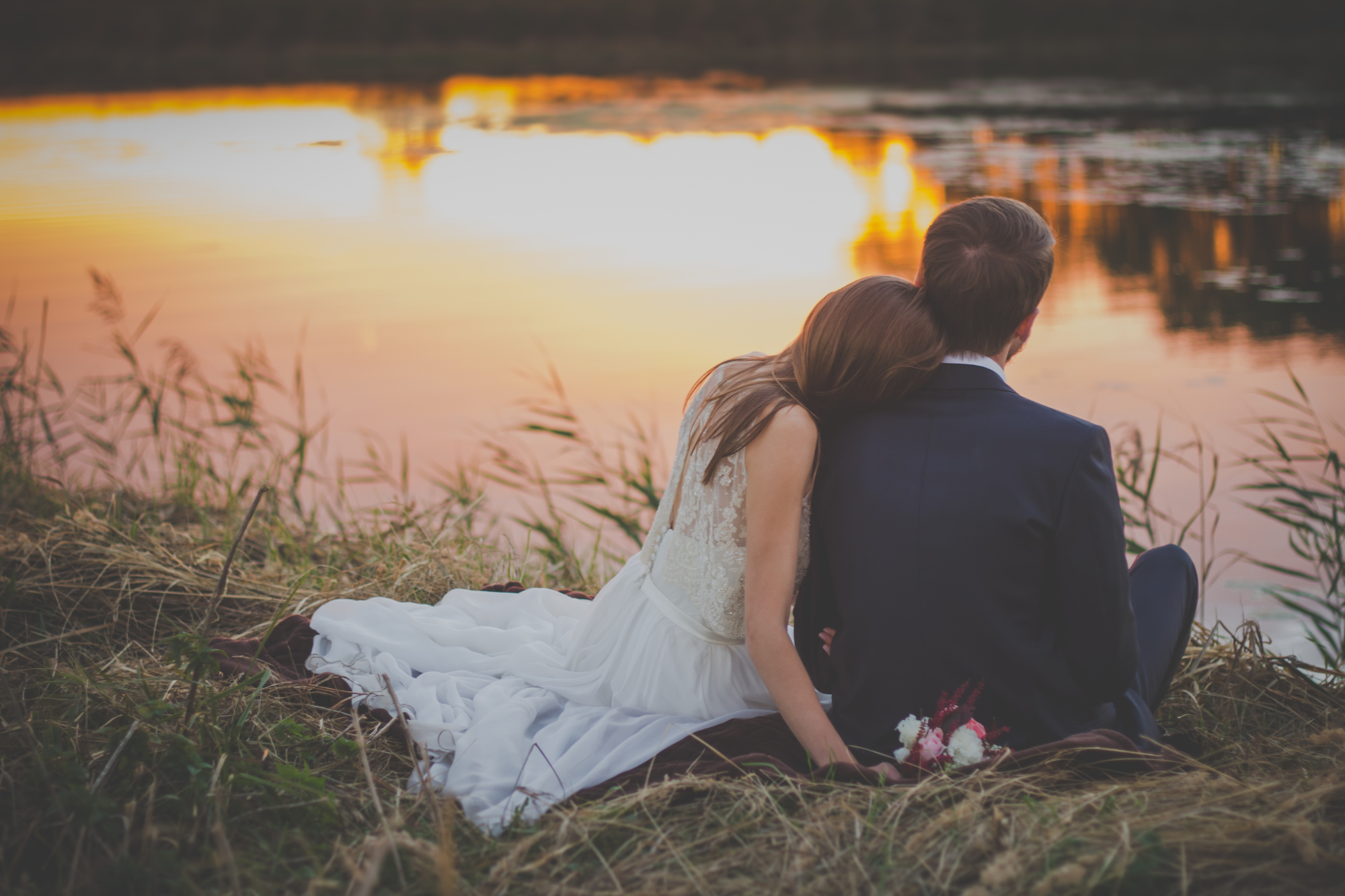 Brude and groom sitting on river bank together during sunset. Blind Belief In Romantic Quotes Could Destroy Your Marriage