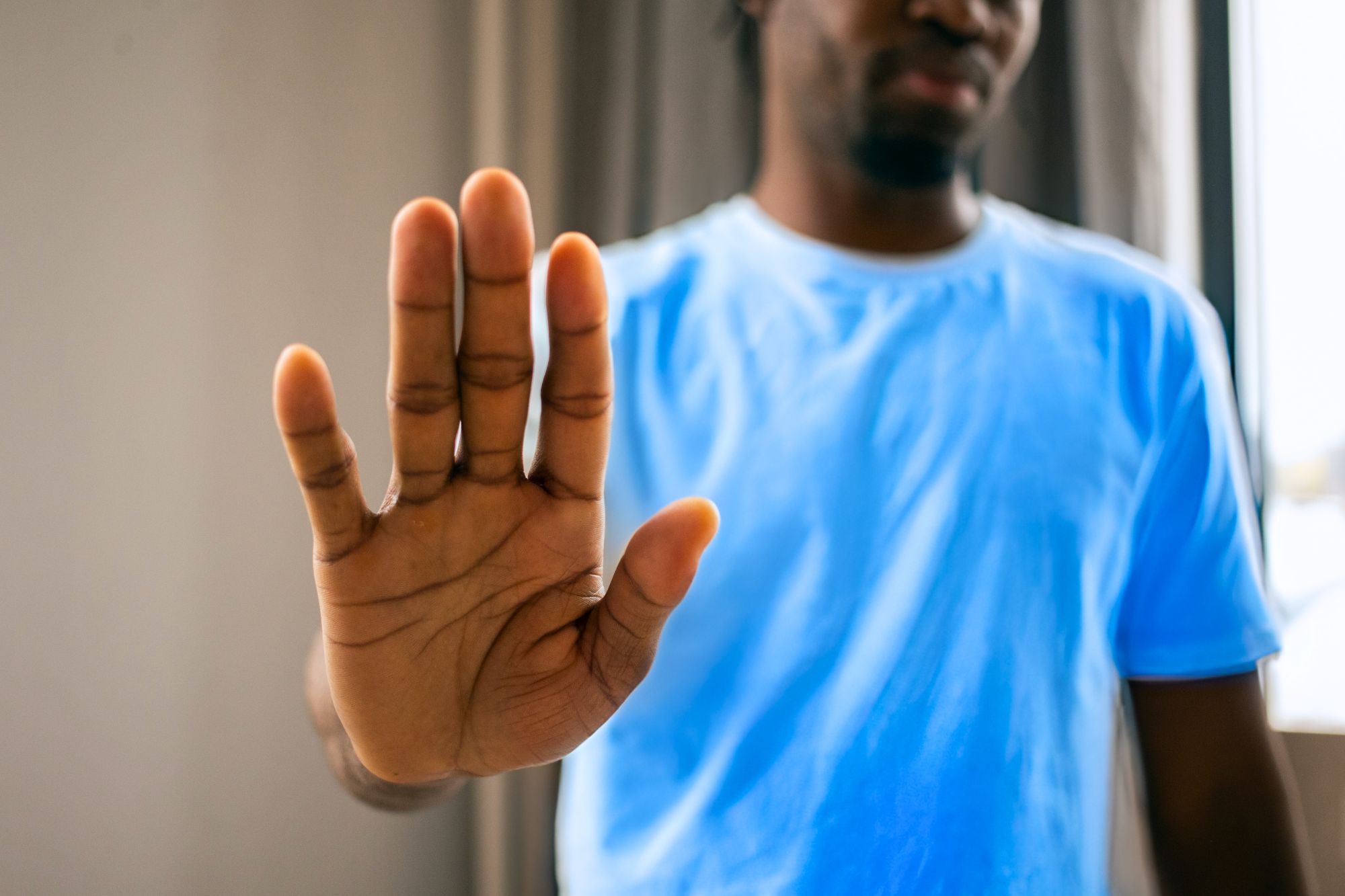 Man in blue shirt stretches his hand out to "stop" as he's considering how to deal with sh*t people say when you're getting divorced.