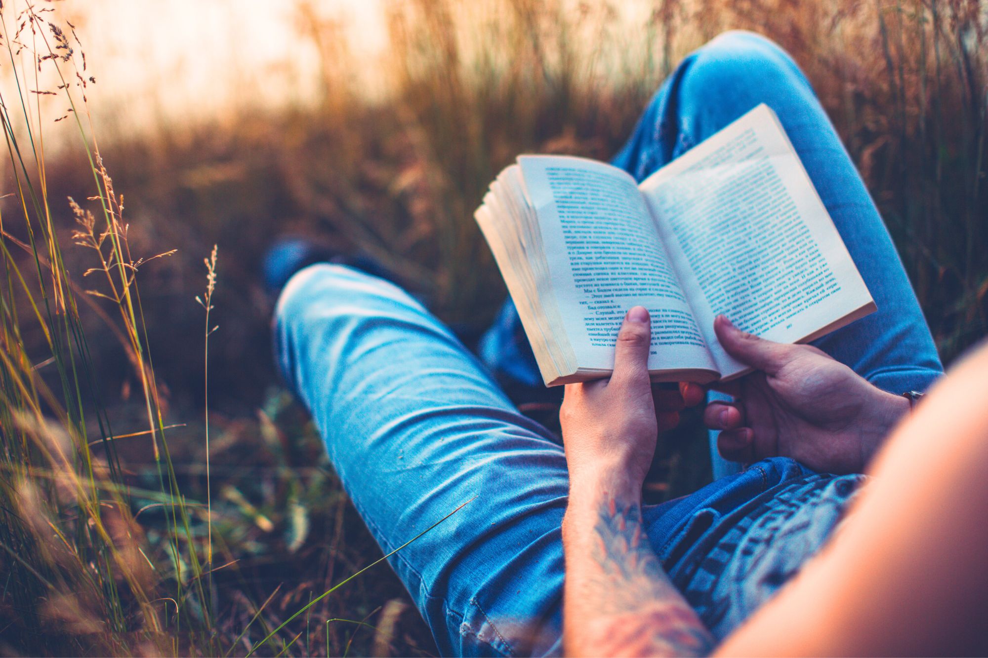 Man resting in grass reading a book about the ways to finally stop wasting your time hating your ex