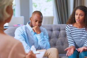 Husband and wife in counseling with a therapist taking notes- wife is asking 'why do married men cheat and stay married'?