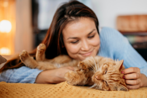 Woman in blue petting orange tabby cat on orange bedspread.Healing from divorce, overcoming lonliness.