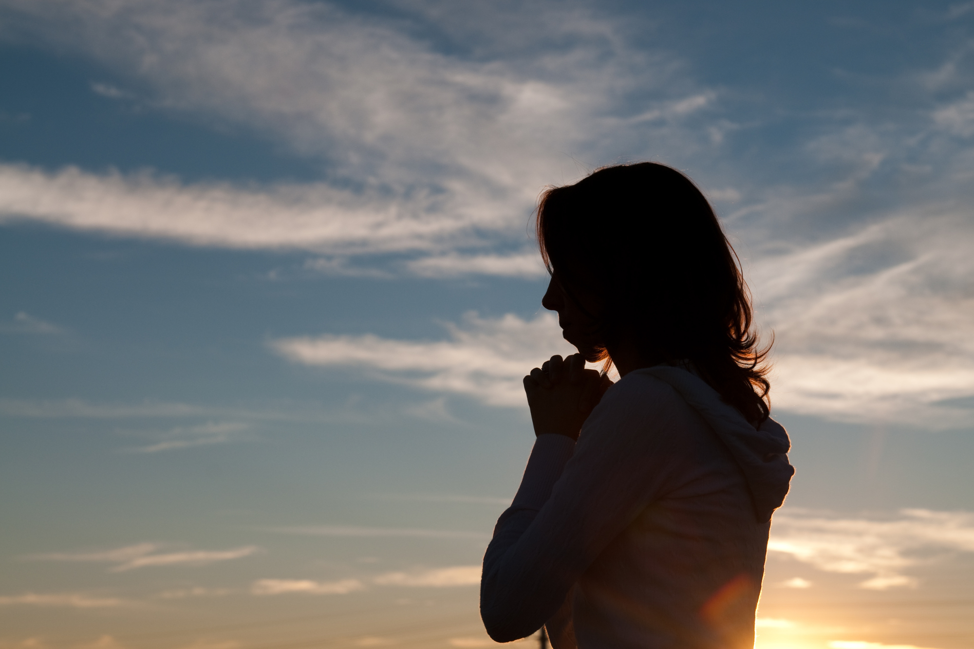 Silhouette of women with clasped hands in front of a sunset/sunrise. How to stay sane when your spouse has filed for divorce.