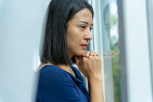 A sad woman in blue looking out the window as she contemplates how to survive infidelity and divorce.