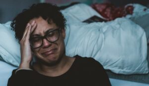 Woman sitting on the floor by her bed sobbing with grief after a divorce.