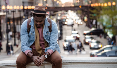 Man wearing a jeans jacket sitting and hanging his head.