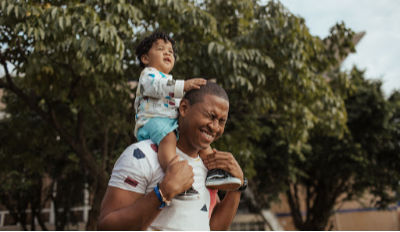 Dad who knows the secrets of co-parenting for divorced parents carrying his son on his shoulders.