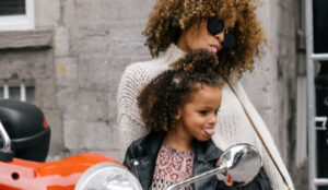 Mother and daughter sitting on a moped making faces in the mirror.