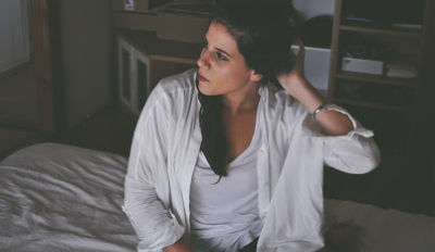 Woman sitting on her bed wondering if she should stay in her miserable marriage or divorce.