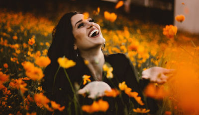 Woman sitting in a field of flowers laughing about these funny, inspirational quotes about life and happiness.