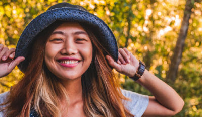 Genuinely happy, smiling woman wearing a gray t-shirt and blue hat.