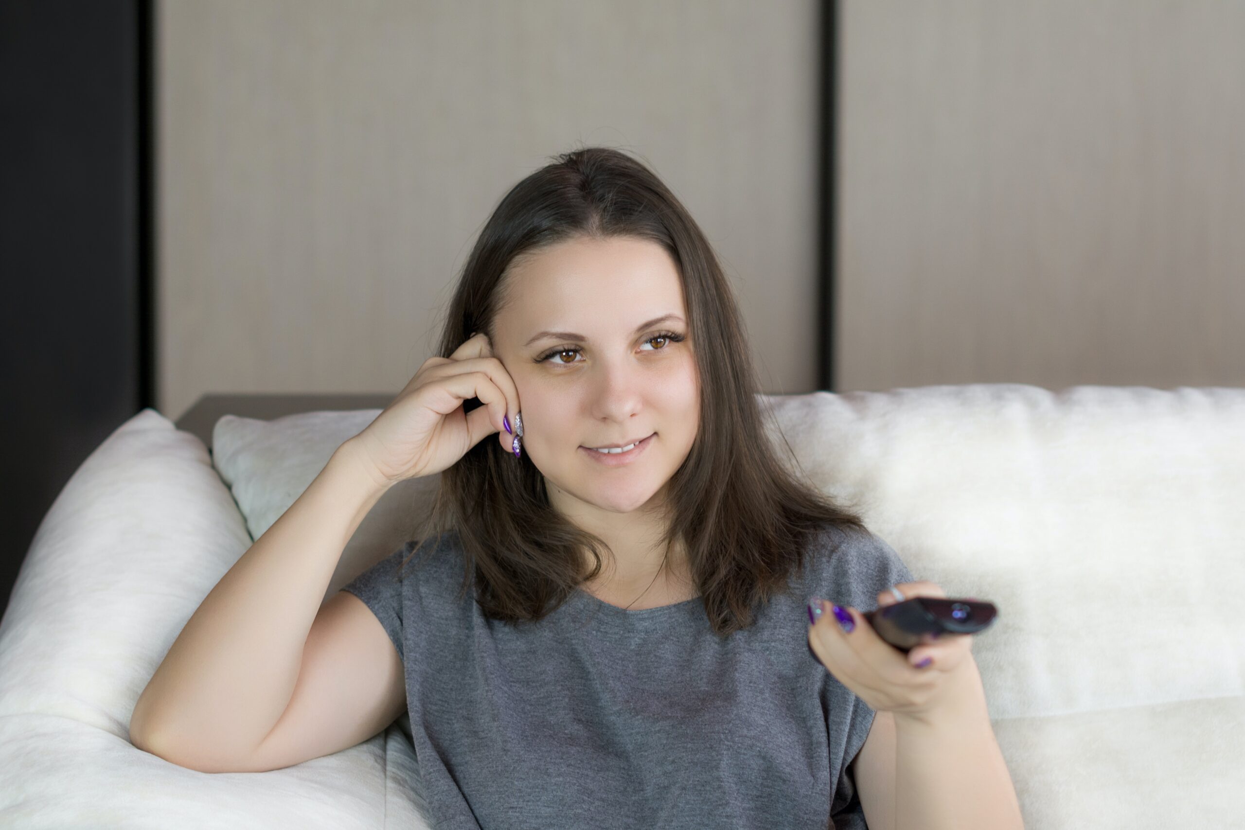 Woman sitting on her sofa using her remote to select a life-after-divorce movie to watch.