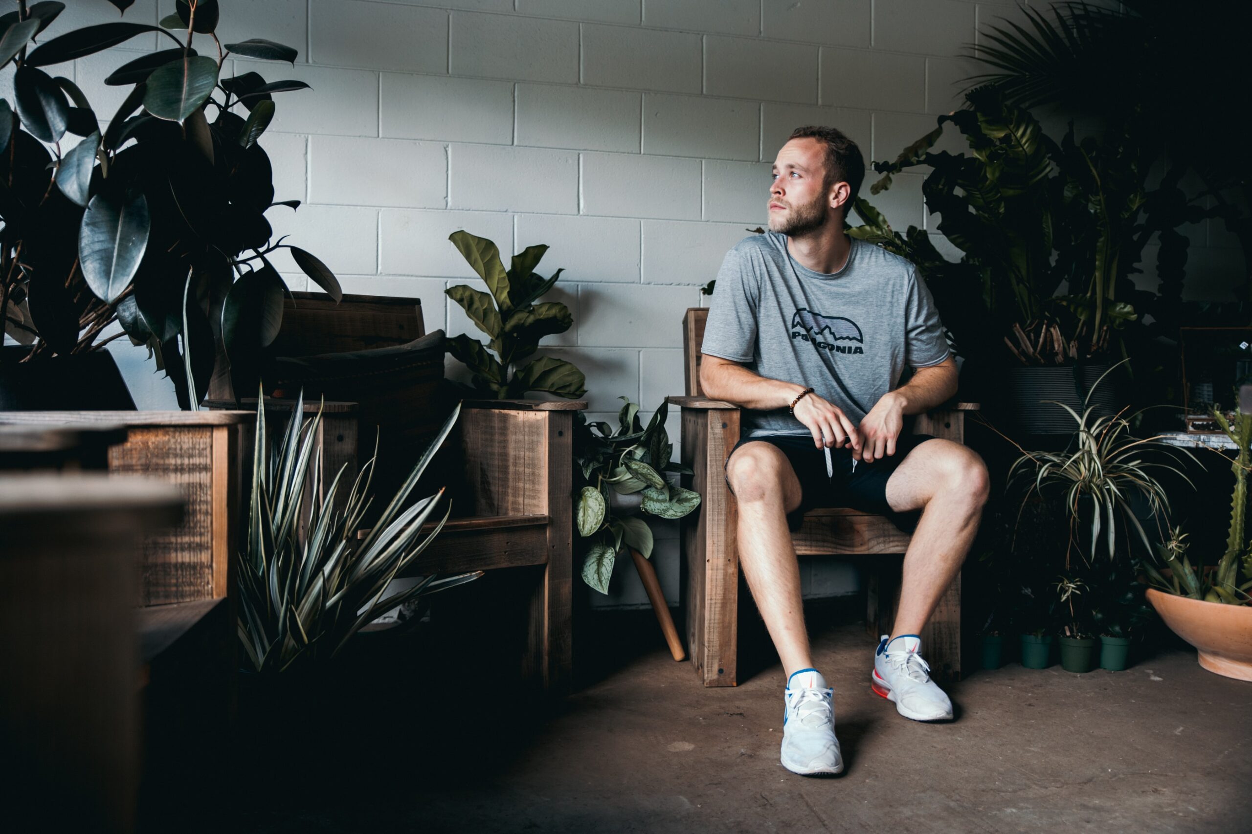 Man sitting in a room of potted plants thinking about being self-aware.