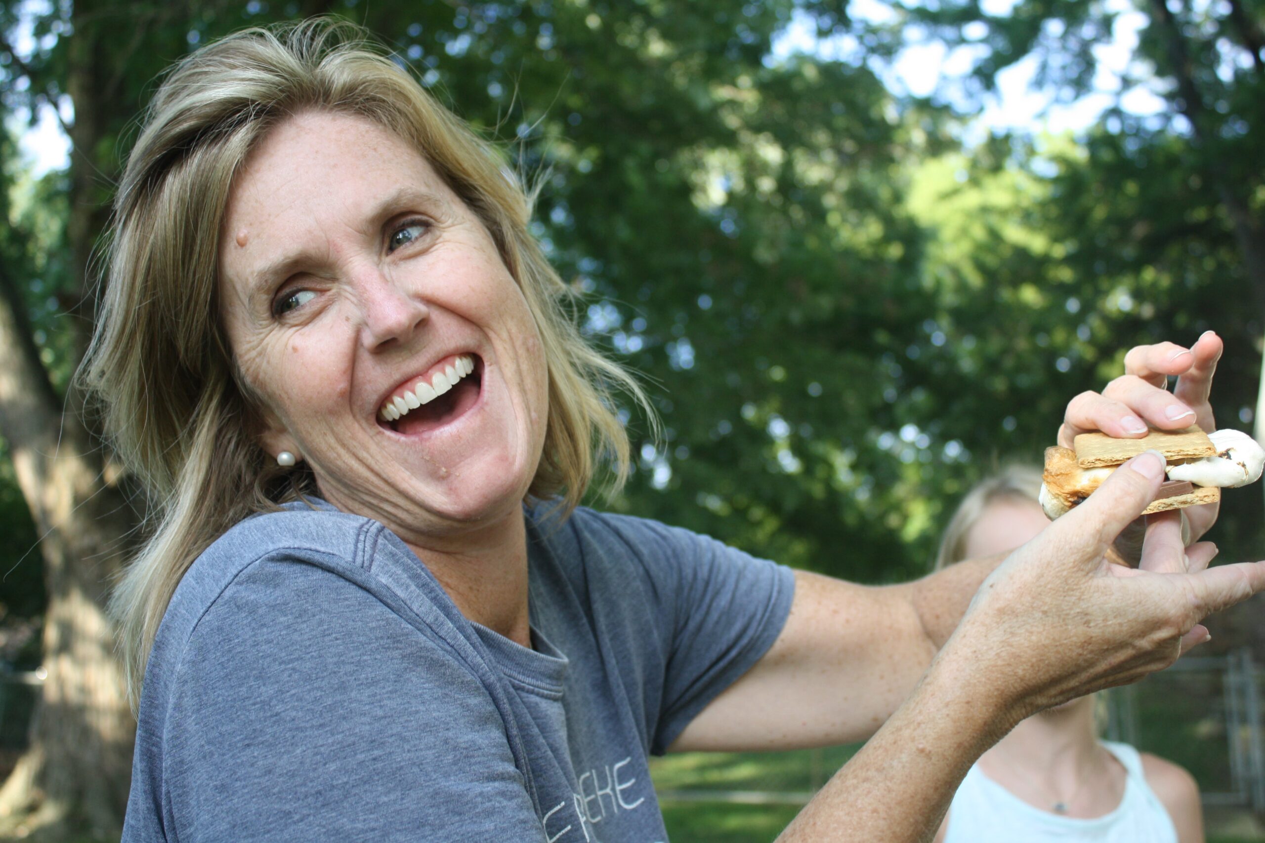 Woman laughing as she struggles with holding a s’more.