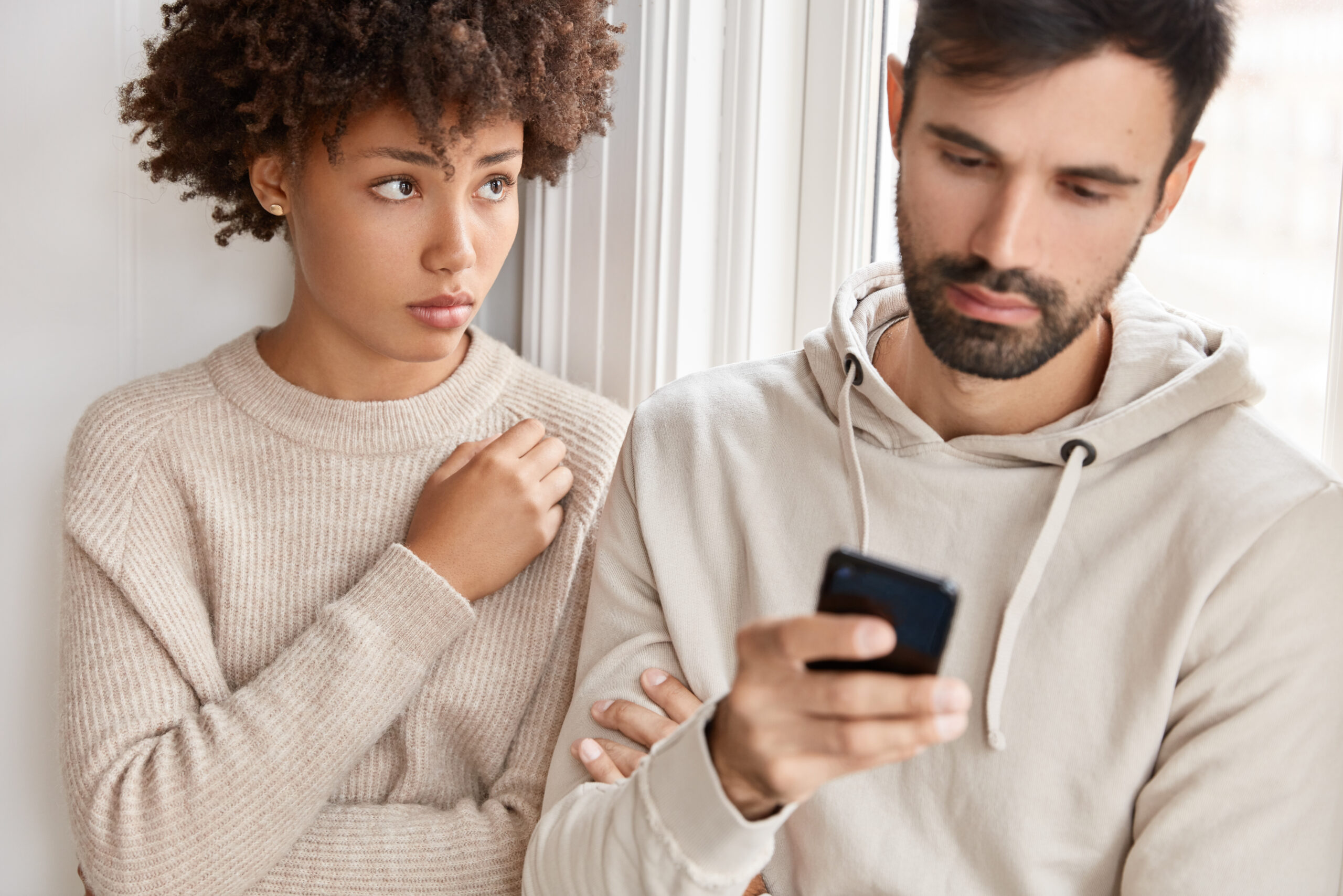 Woman looking forlornly at her husband who is engrossed in his phone.