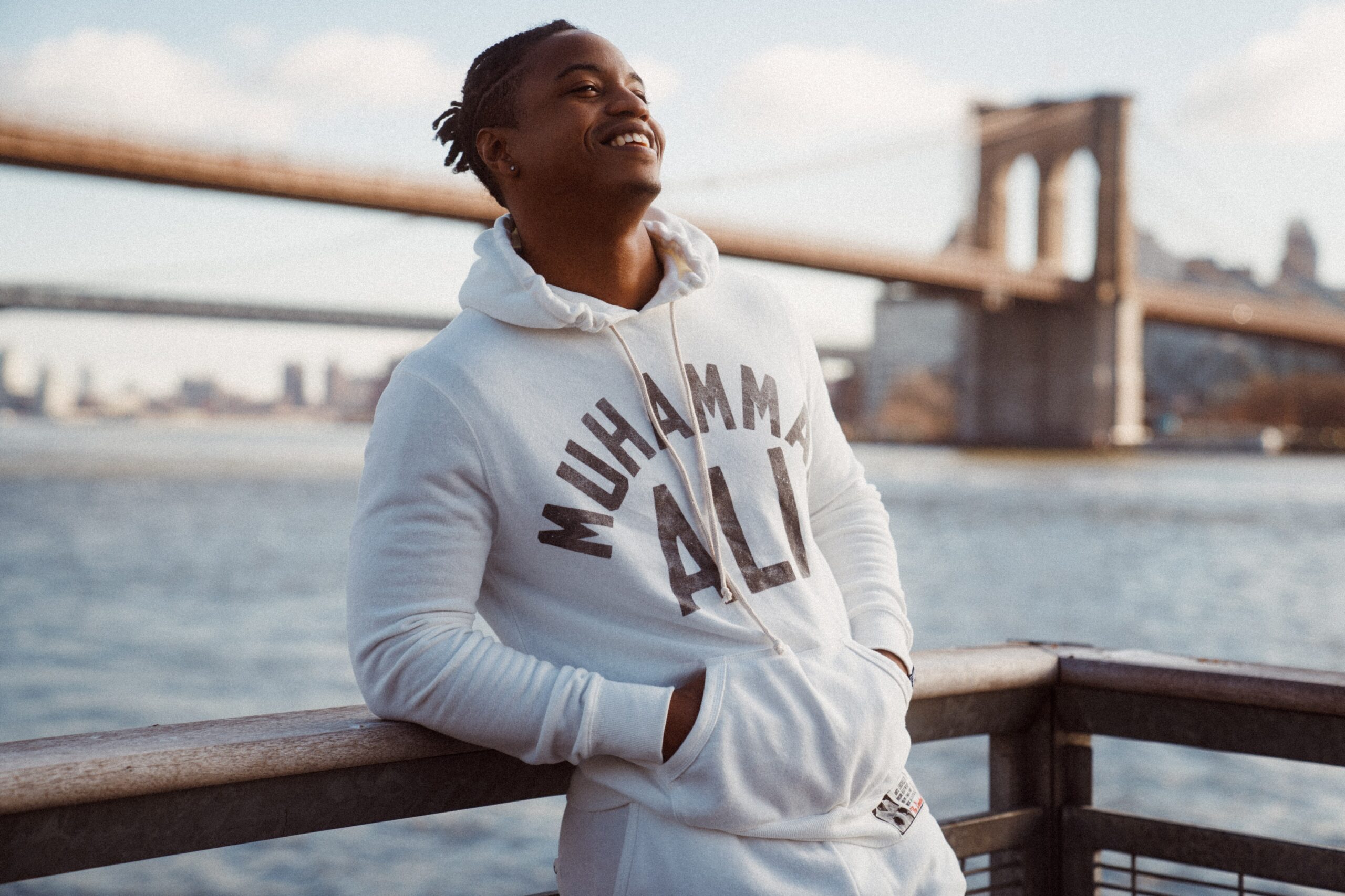 Man smiling and enjoying his happy life while leaning on a railing with NYC in the background.