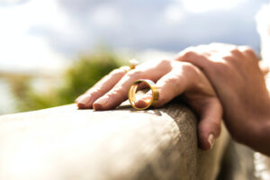 Woman holding her husband’s wedding ring pinned against a wooden ledge.