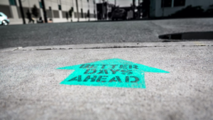 Better days ahead” printed inside a green arrow on pavement.