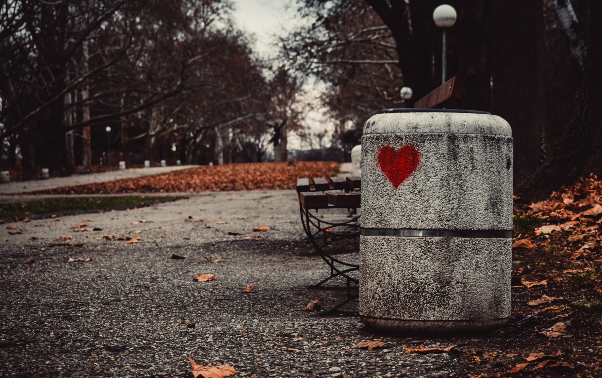 Gray cement trashcan with a red heart painted on it.