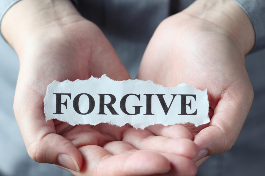 Woman holding a torn piece of paper with the word forgive printed on it.