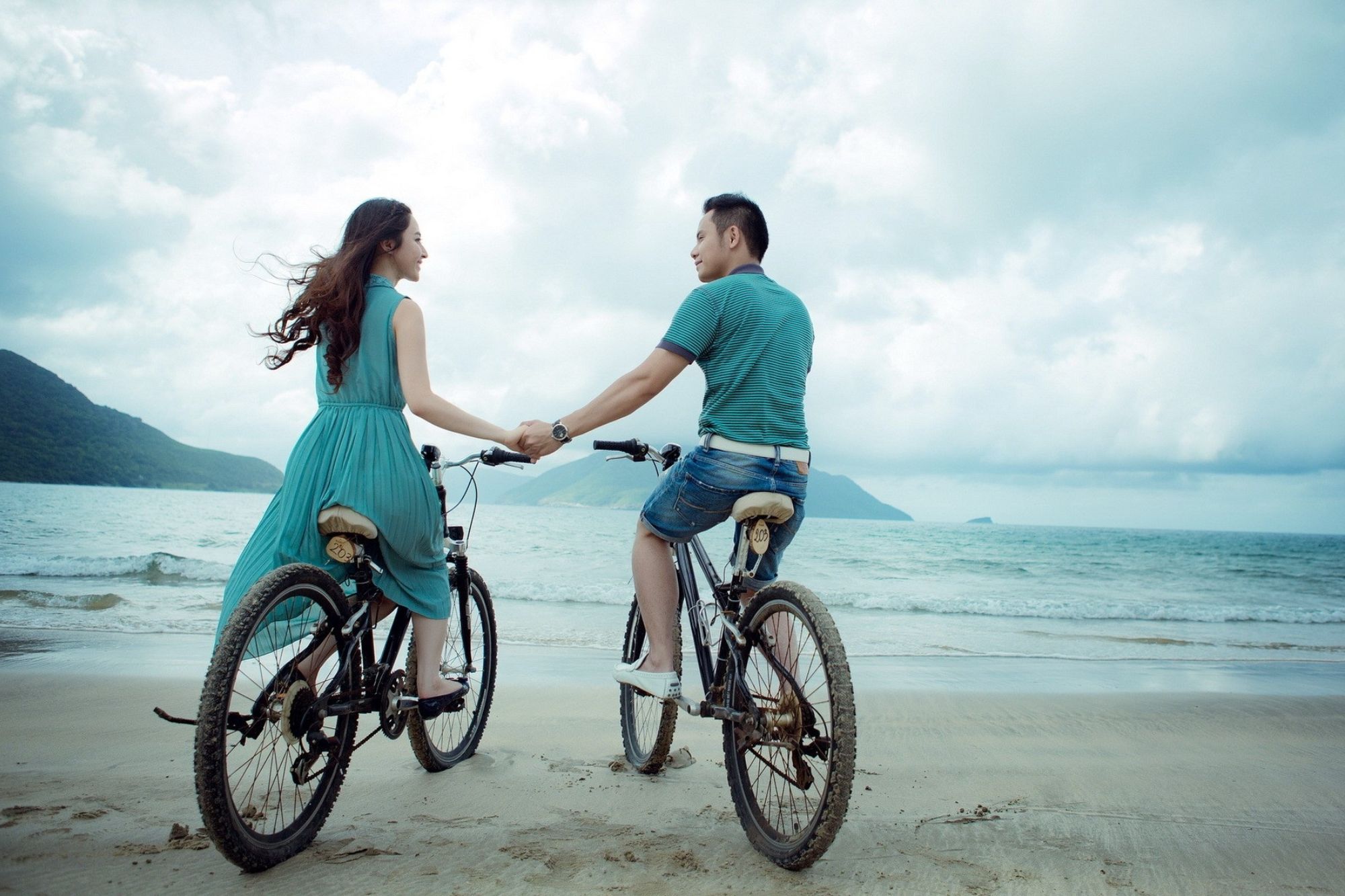 Couple pausing in their bike ride along a beach to hold hands.