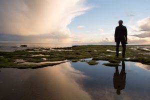 Reflection of Man in tidepools at the ocean with clouds