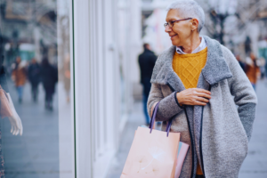 Older woman in golden sweater smiling confidently while window shopping on busy sidewalk